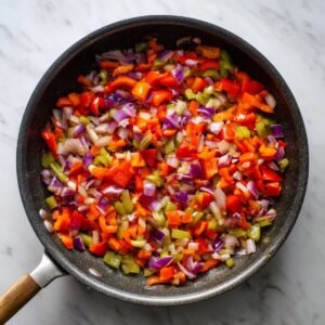 "Sautéed diced red onions, green, and red bell peppers in a skillet, glistening as they soften over heat."