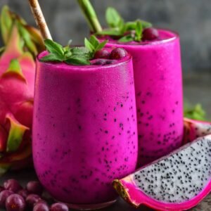 "Two glasses of bright pink dragon fruit smoothies garnished with mint leaves and berries, served with fresh dragon fruit slices."