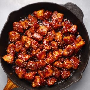 Skillet of Korean glazed chicken pieces topped with sesame seeds.