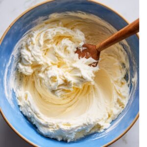 A blue bowl with creamy, whipped cupcake batter mixed smooth with a wooden spoon.