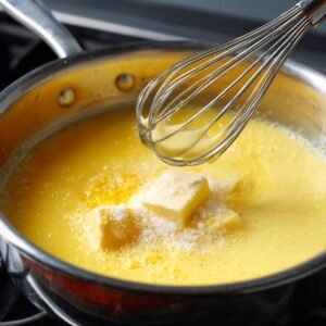 "Whisk mixing lemon filling in saucepan with butter and sugar melting into the mixture."