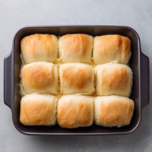 A tray of freshly baked, fluffy golden crescent rolls in a rectangular baking dish.