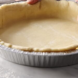 A baking pan lined with unbaked dough pressed evenly along the bottom and sides.