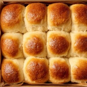 Golden, fluffy baked rolls in a pan, their tops shiny and perfectly browned, fresh from the oven.