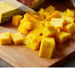 Fresh squash being chopped into large chunks on a wooden cutting board with a knife.