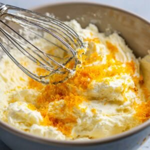 Mixing bowl with creamy butter mixture topped with fresh orange zest and a whisk.