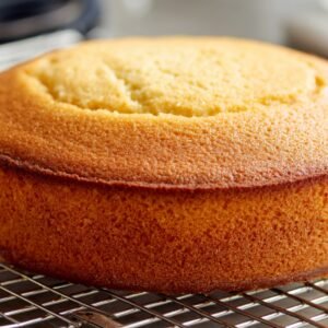 Freshly baked round orange cake cooling on a wire rack, golden brown with a smooth top.