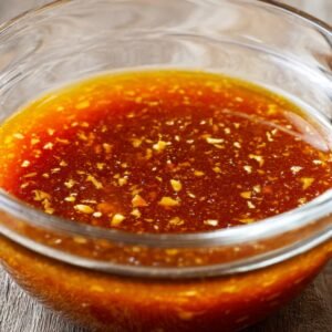 A glass bowl filled with freshly prepared orange sauce, containing visible garlic and zest.