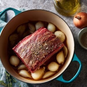 "Uncooked chuck roast seasoned with salt and pepper in a Dutch oven with pearl onions and broth."