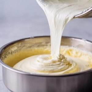 Thick and fluffy cheesecake filling being poured into a baking pan, smooth and creamy texture visible.