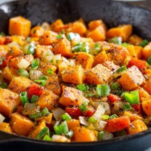 Colorful sweet potato hash in a skillet with diced onions, bell peppers, and green onions sprinkled on top.