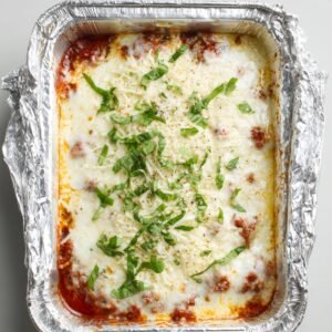 "Freshly baked zucchini lasagna topped with melted mozzarella cheese and garnished with chopped basil in a foil baking dish."