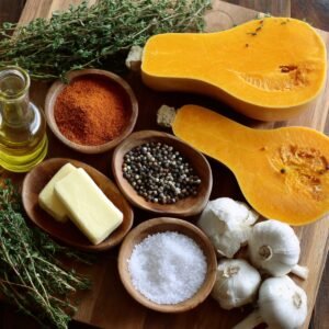 "Ingredients for roasted butternut squash including fresh thyme, garlic, olive oil, butter, spices, and halved squash."