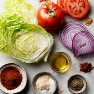 "Sliced red onion, tomato, romaine lettuce, olive oil, and various spices arranged on a light kitchen surface for burger toppings."