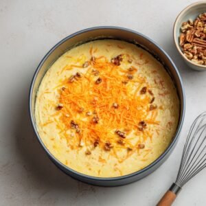 Baked carrot cake cheesecake topped with shredded carrots and walnuts in a springform pan.