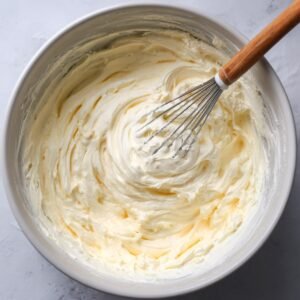 Bowl of creamy cheesecake batter being whisked until fluffy.
