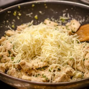 Rolled flour tortillas filled with chicken, placed in a baking dish, and topped with shredded cheese over a creamy white sauce.