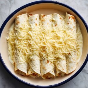 A skillet filled with cooked chicken pieces mixed with shredded cheese and herbs, being prepared for enchilada filling.