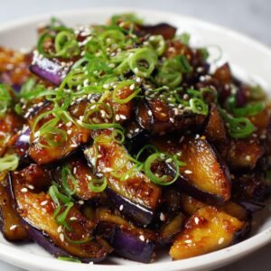 A plate of glazed stir-fried Japanese eggplant garnished with sesame seeds and thinly sliced green onions.