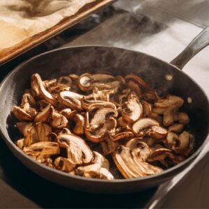 Skillet with golden-brown mushrooms sizzling and steaming during sautéing.
