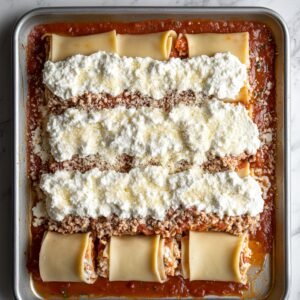 "Unbaked lasagna roll ups filled with meat sauce, neatly arranged in a white baking dish and garnished with a few parsley leaves."