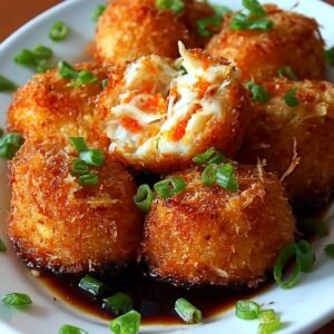 A plate of crispy Rangoon crab bombs, topped with green onion garnishes, with one bomb cut in half to reveal its crab and filling.
