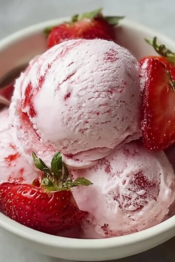 A bowl of homemade strawberry ice cream with a scoop of pink ice cream, garnished with fresh strawberries.