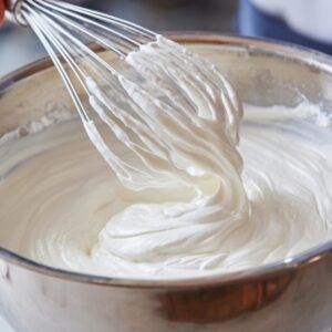 A whisk gently mixing a bowl of whipped cream, creating a smooth, fluffy texture, showing the creamy consistency of the mixture.