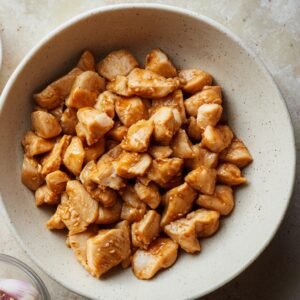 A bowl of diced chicken pieces coated in a light brown marinade, ready to be cooked.
