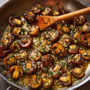 A skillet of sautéed mushrooms with garlic and parsley, cooking in a flavorful butter and herb mixture.