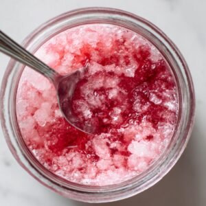 A jar filled with crushed ice and a pink syrup, likely a base for a fruity ice dessert.