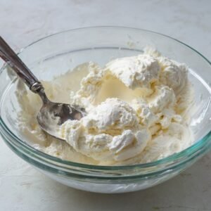 A close-up of a creamy, fluffy mixture in a glass bowl, likely whipped cream or a base for a dessert.