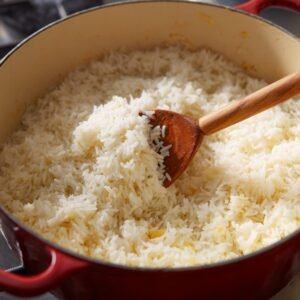 A pot of freshly cooked white rice being stirred with a wooden spoon, showing its light and fluffy texture.