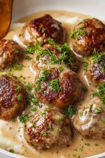 "Swedish meatballs served with a creamy gravy over mashed potatoes, garnished with fresh herbs."