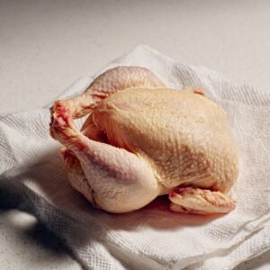 A raw whole chicken resting on a paper towel, ready to be seasoned or cooked.